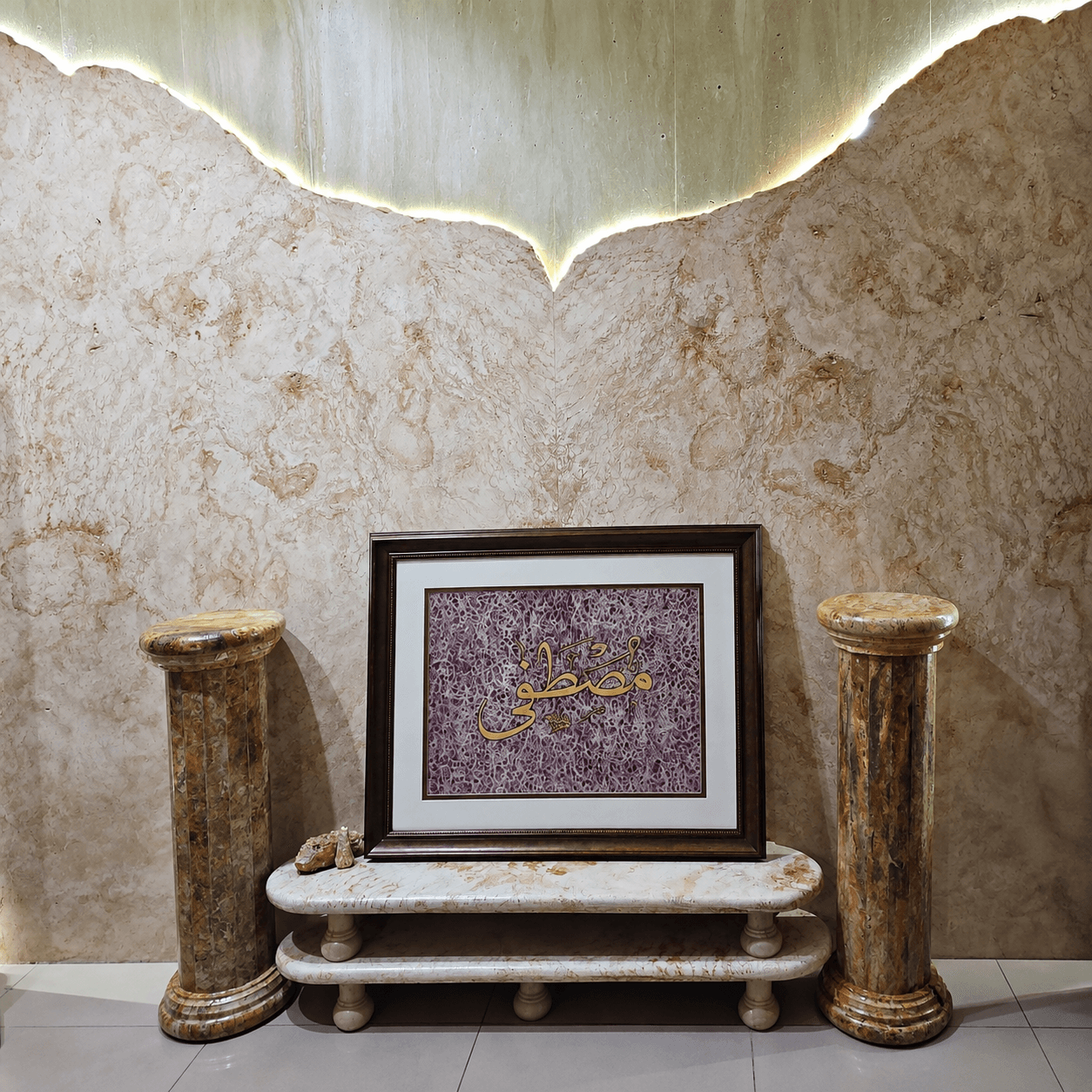 Framed Arabic calligraphy flanked by two onyx columns beneath a backlit ceiling feature