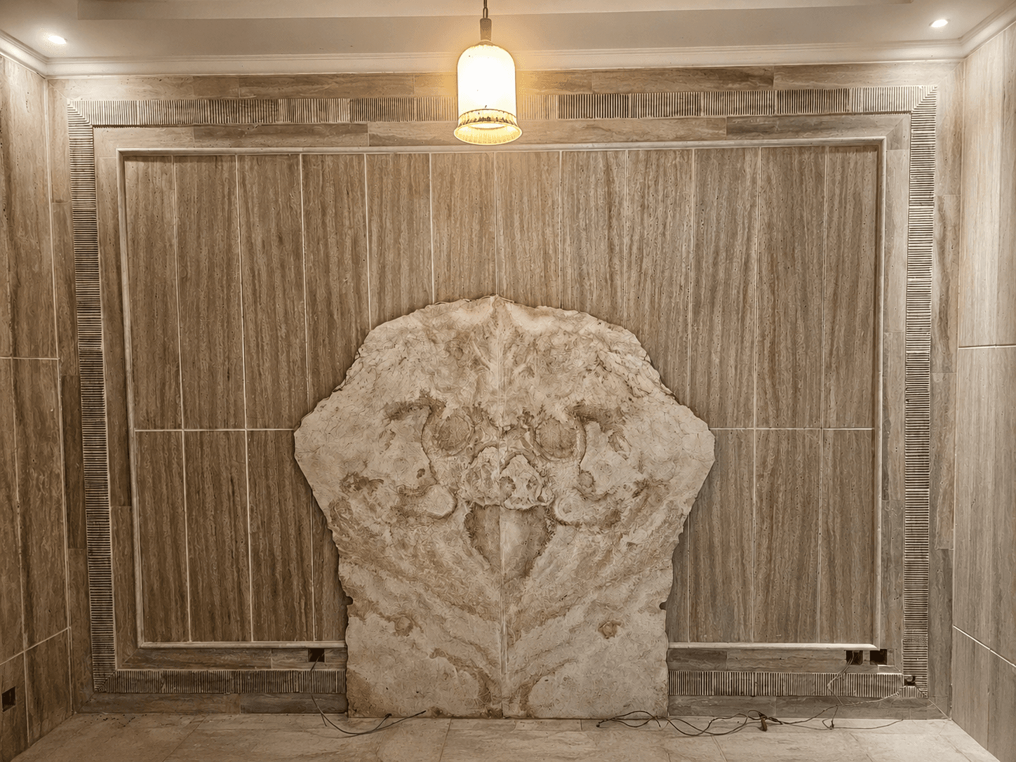 Foyer with a wooden door, travertine walls, and a dark and gold stone floor inlay