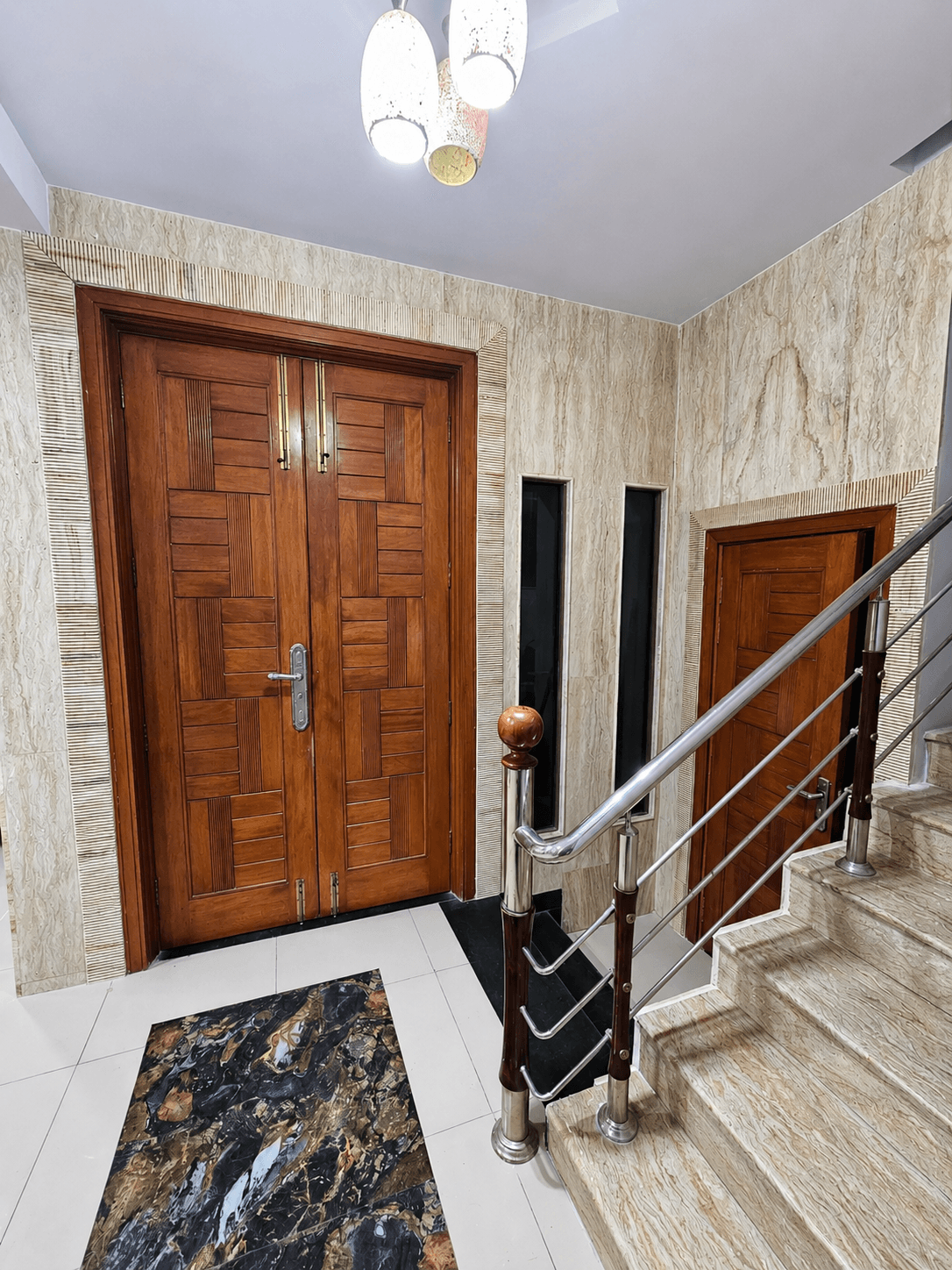 Grand entrance hall with a carved wooden double door, a secondary staircase door, and a marble floor inlay rug
