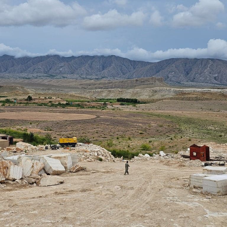 Wide quarry landscape with mountains, raw blocks, and a worker walking the site