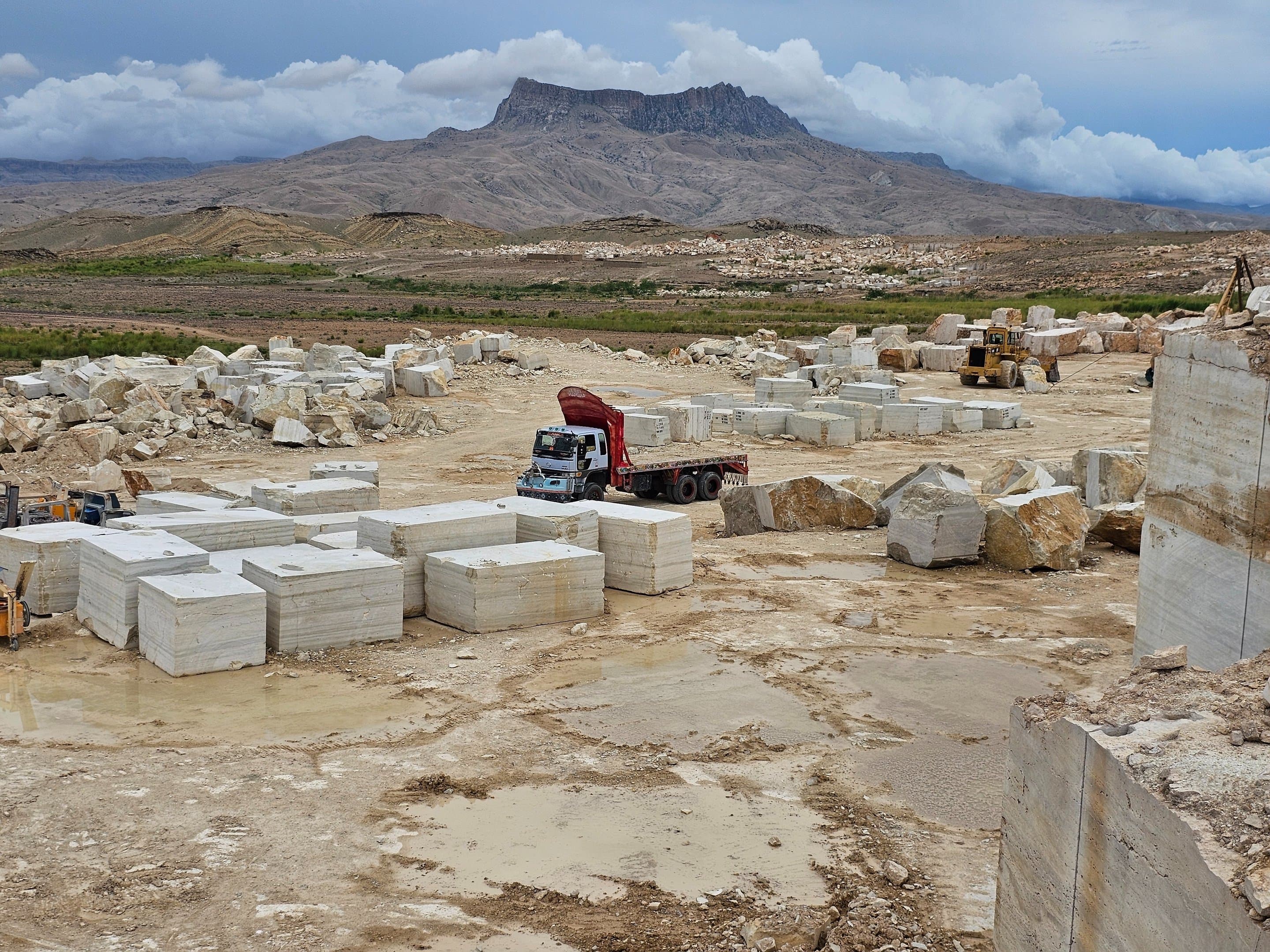 Quarry landscape in Loralai with mountain peak, a loaded truck, and stacked raw blocks