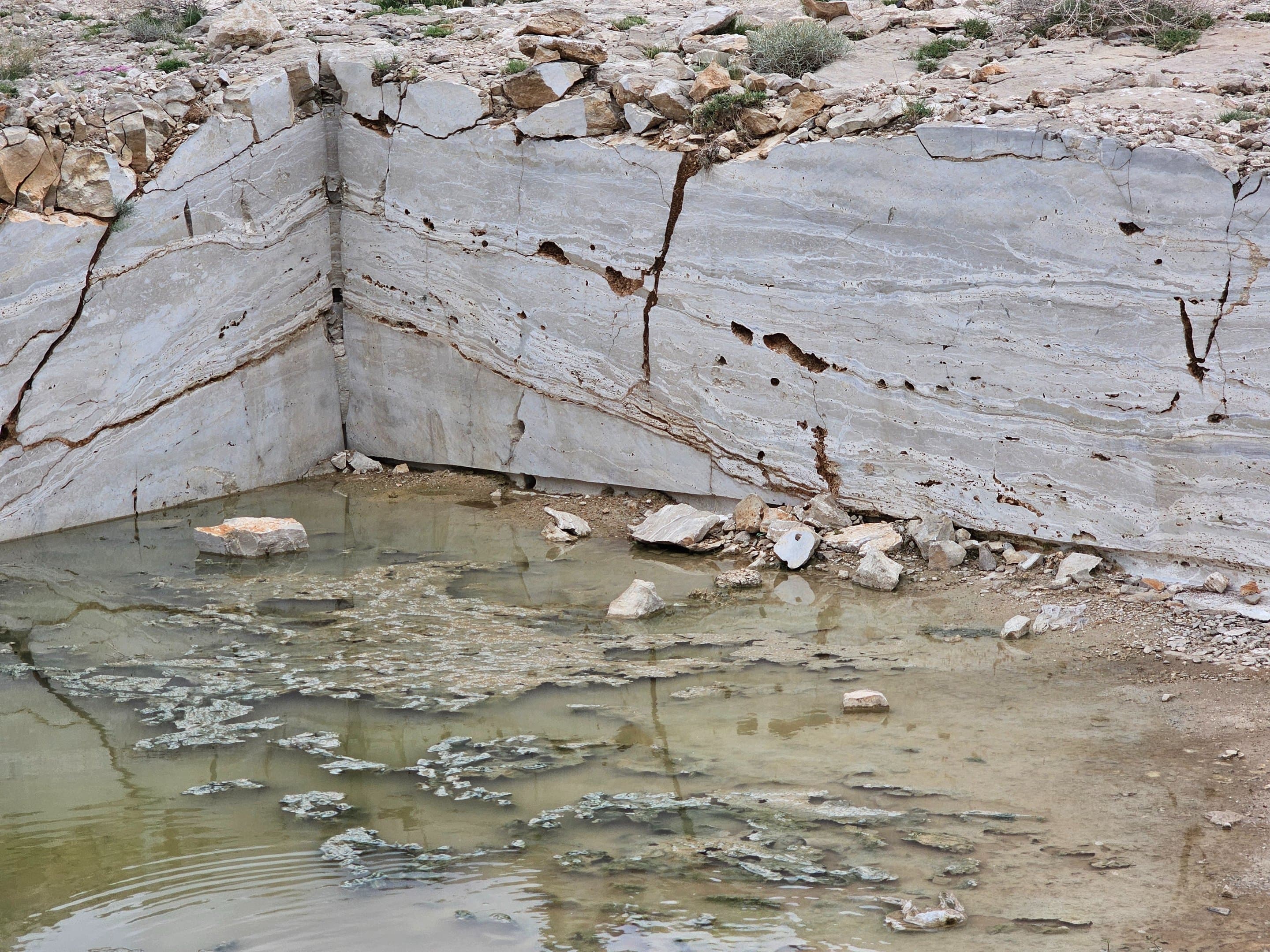 Two stacked raw travertine blocks with a crane visible in the background at the quarry