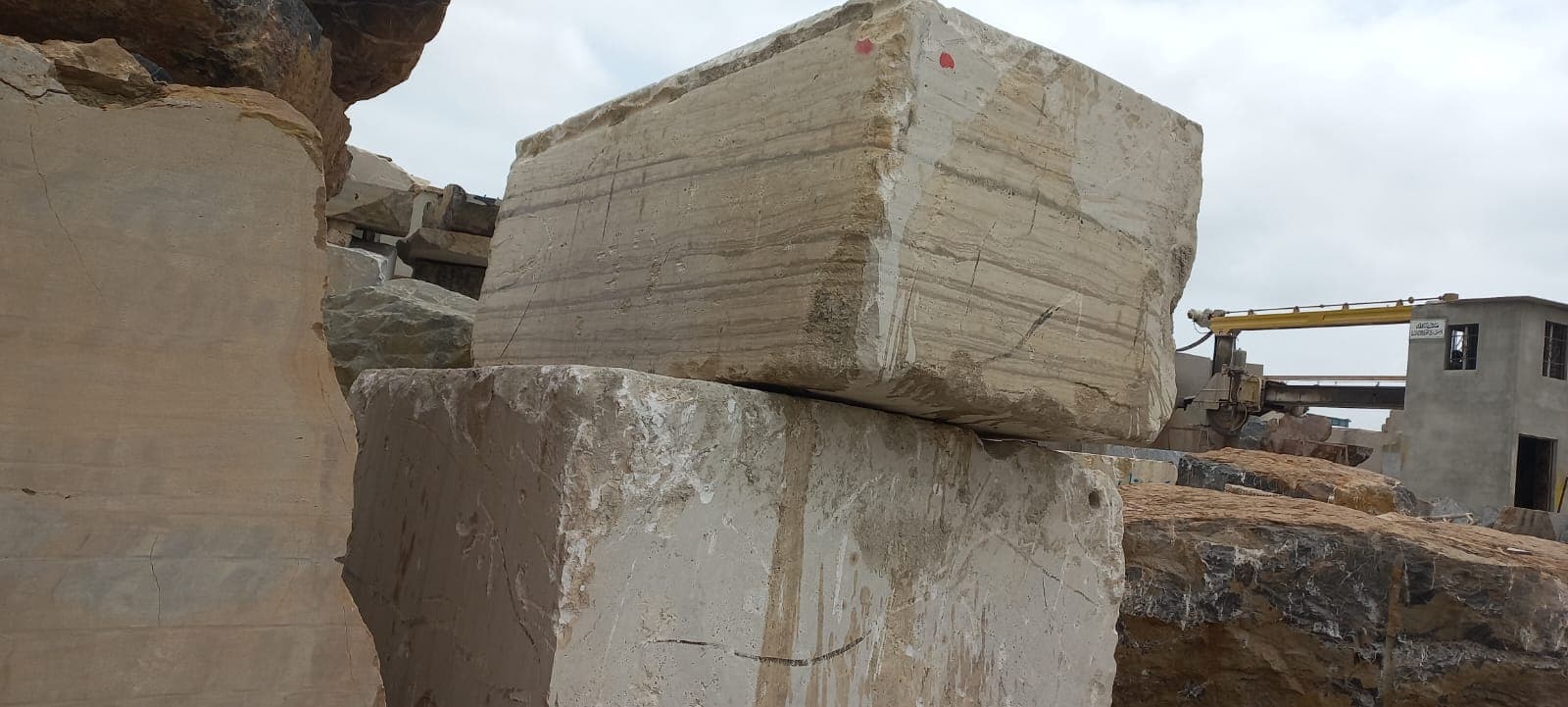Two stacked raw travertine blocks with a crane visible in the background