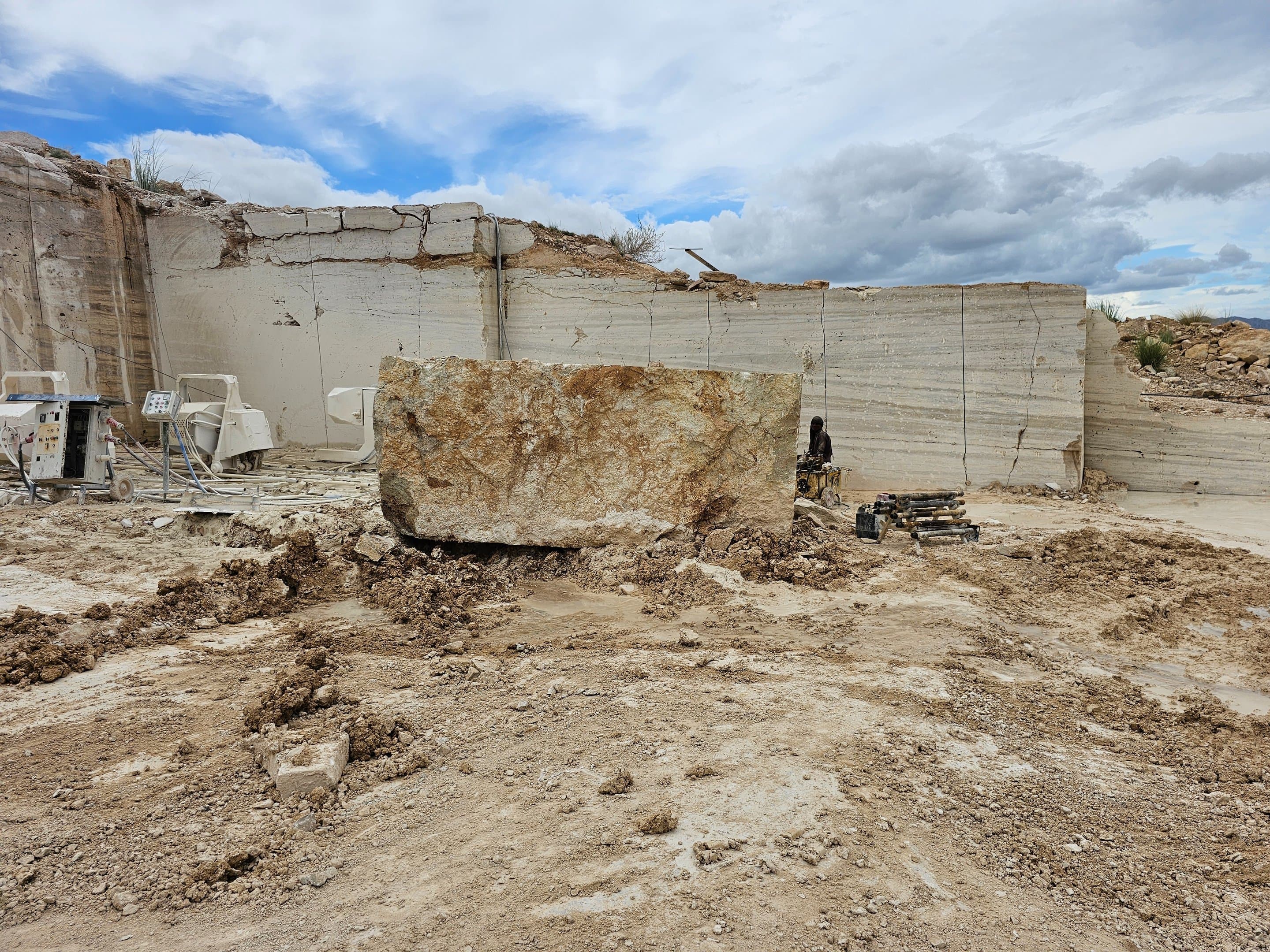 Rough-cut travertine block beside processing machinery at the quarry