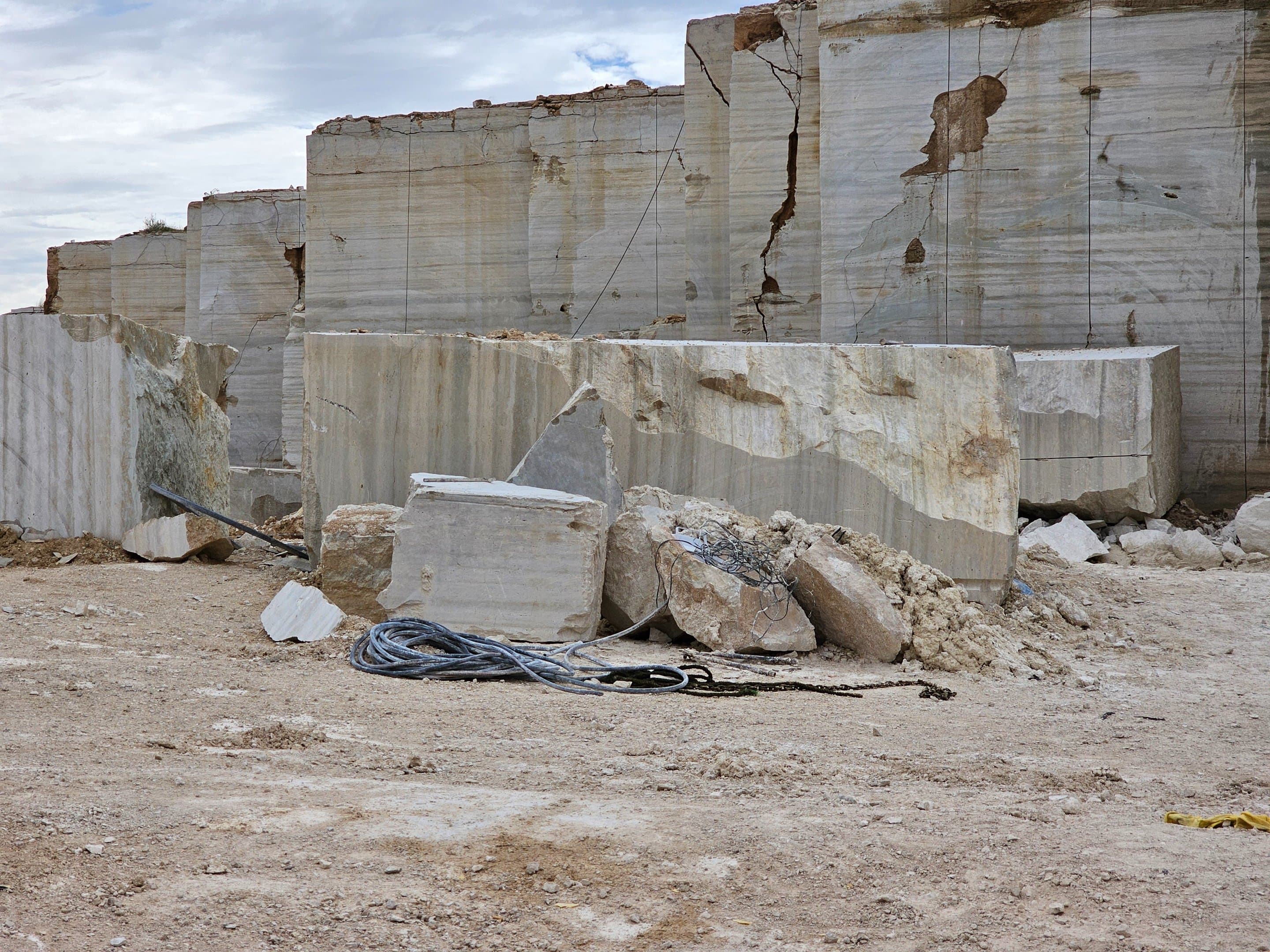 Raw travertine quarry wall with stepped blocks and coiled cable in the foreground