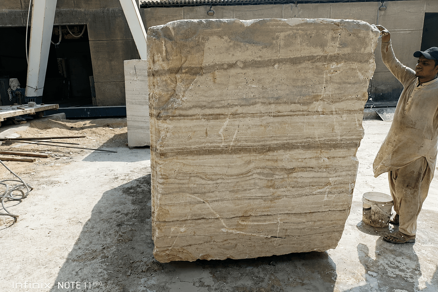 A worker standing beside a freshly quarried raw travertine block, showing its natural scale