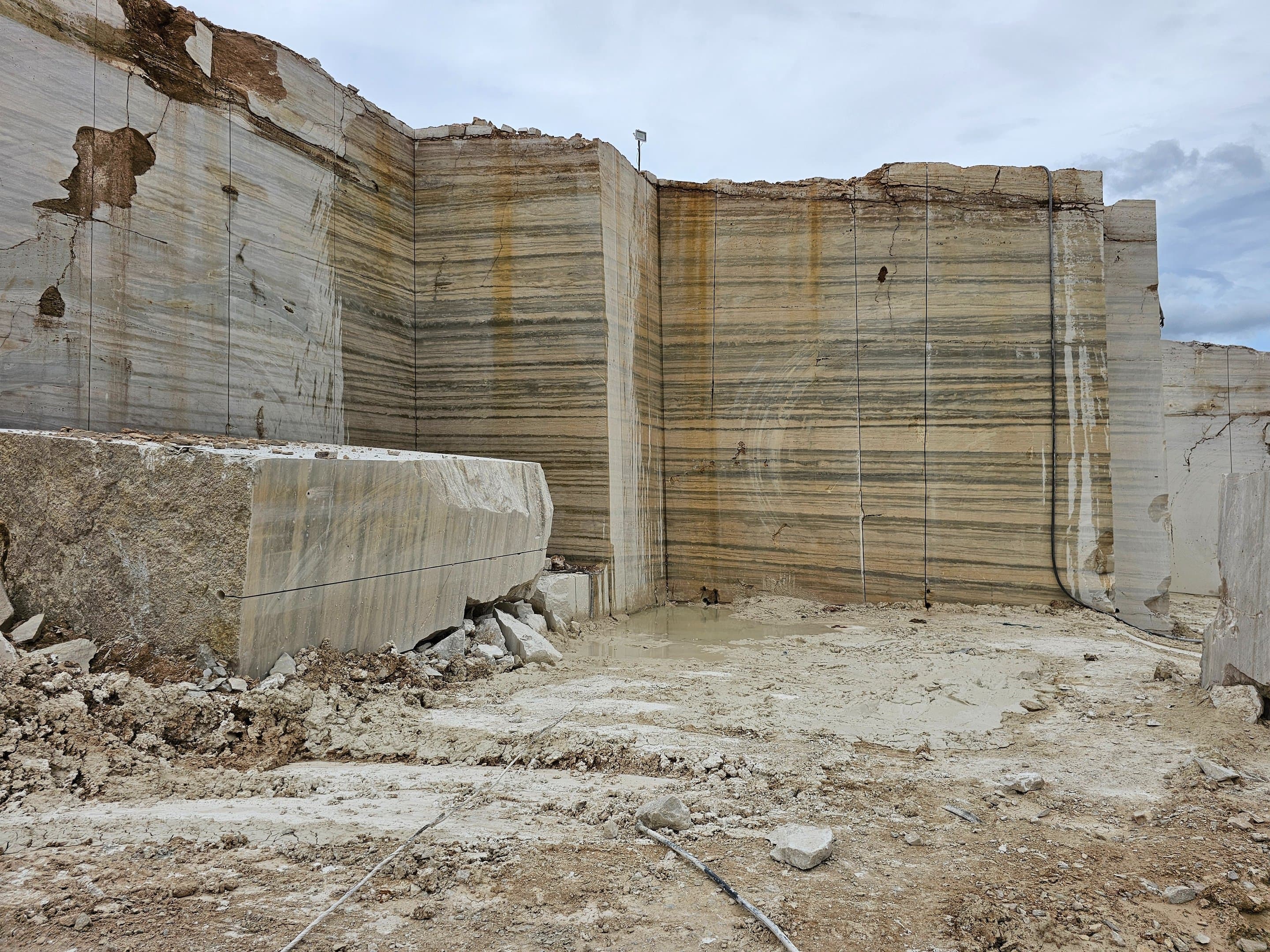 Raw travertine quarry wall in Loralai, Balochistan, showing natural banded stone strata and a reflective water pool